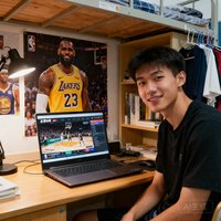 一位大学生模样的年轻男性用户照片，他坐在大学宿舍的书桌前，身后墙上贴着NBA球星海报，桌上放着笔记本电脑，正在通过友博体育观看篮球比赛。